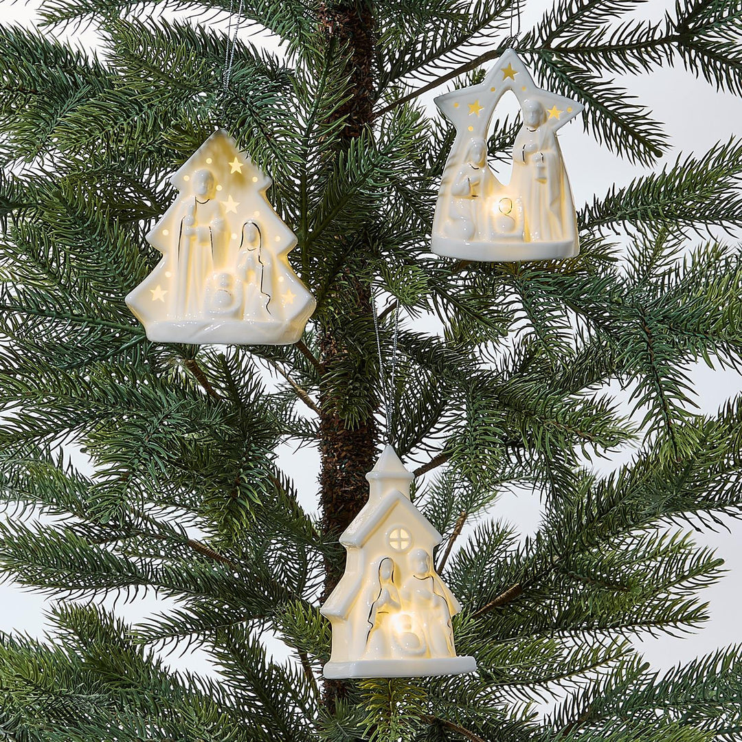 Decorative Christmas tree ornaments shaped like a nativity scene hanging on a tree.