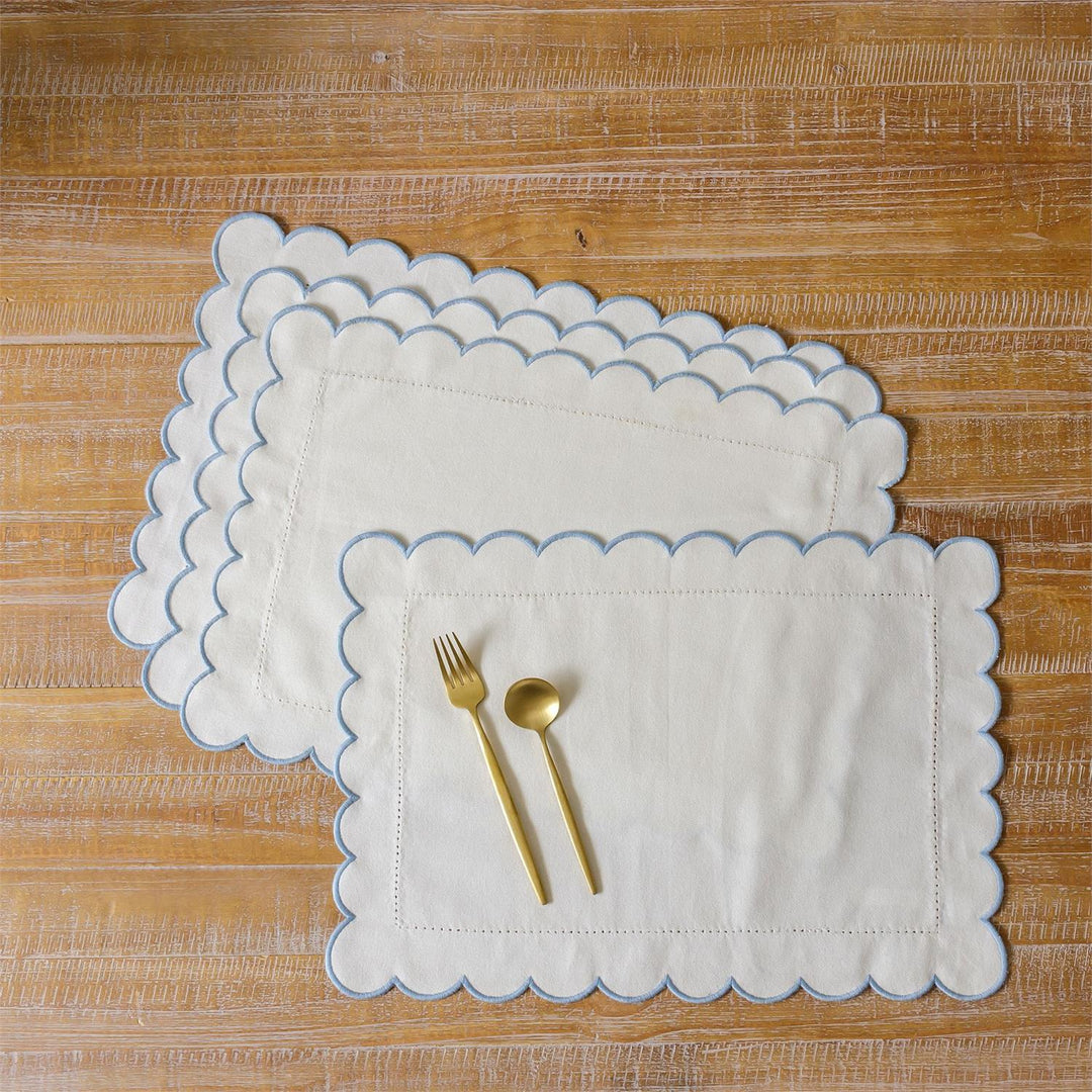 White scalloped placemats with gold cutlery on a wooden surface