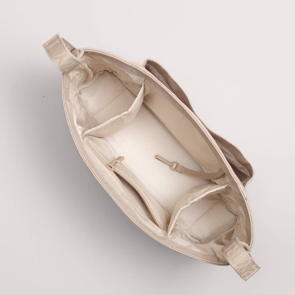 An overhead view of a beige tote bag showing its interior compartments, zippered pockets, and adjustable shoulder straps against a light gray background.