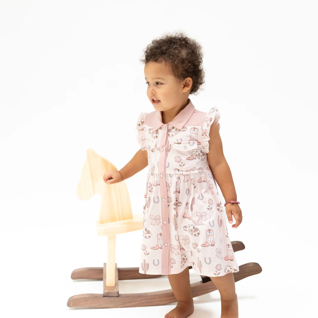 Angel Dear Cowgirl Boots and Bows Western Pearl Snap Dress and Bloomer worn by a baby in a lifestyle view highlighting the cowgirl boots and bows western pearl snap dress and bloomer design