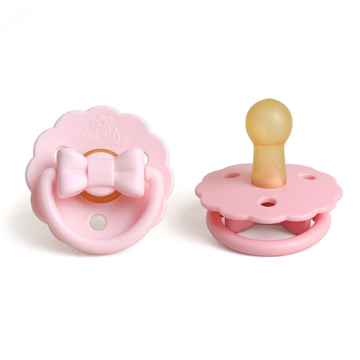 Two pink baby pacifiers with a bow on a white background