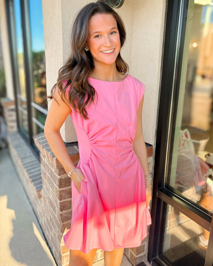 Woman modeling a sleeveless pink mini dress with ruched waist detail and side pockets.