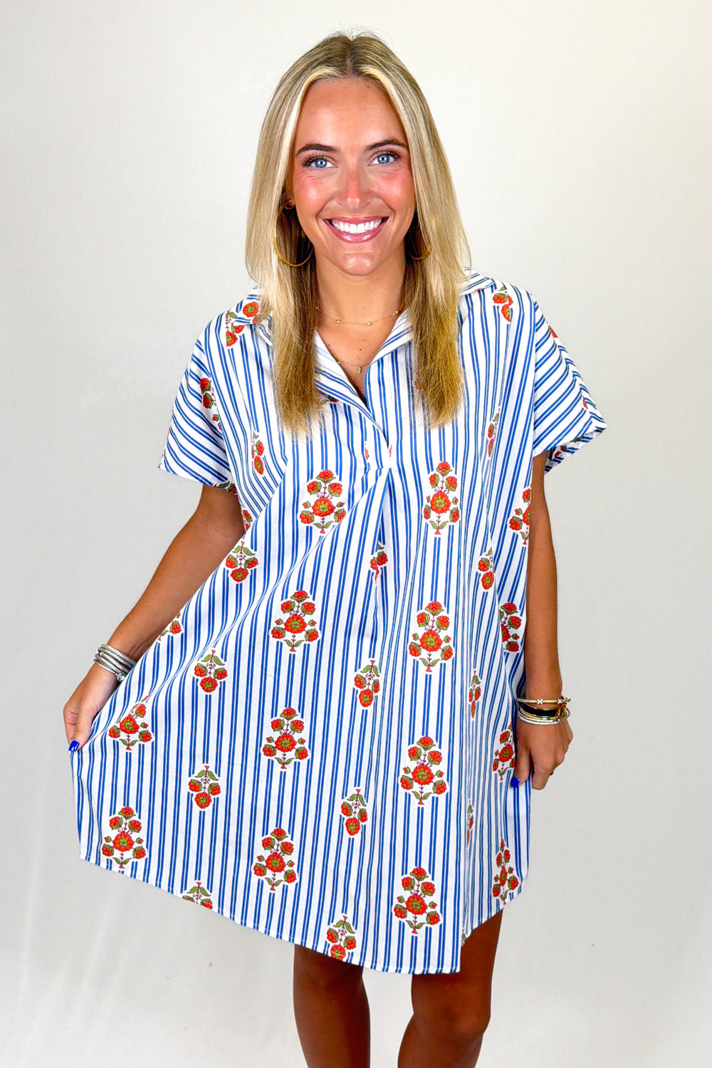 Woman wearing a blue and white striped dress with orange floral patterns on a plain background