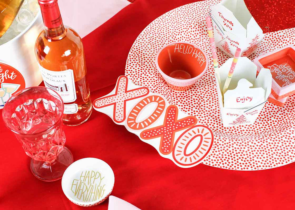 Table setting with a bottle of wine, glasses, and decorative items on a red tablecloth.