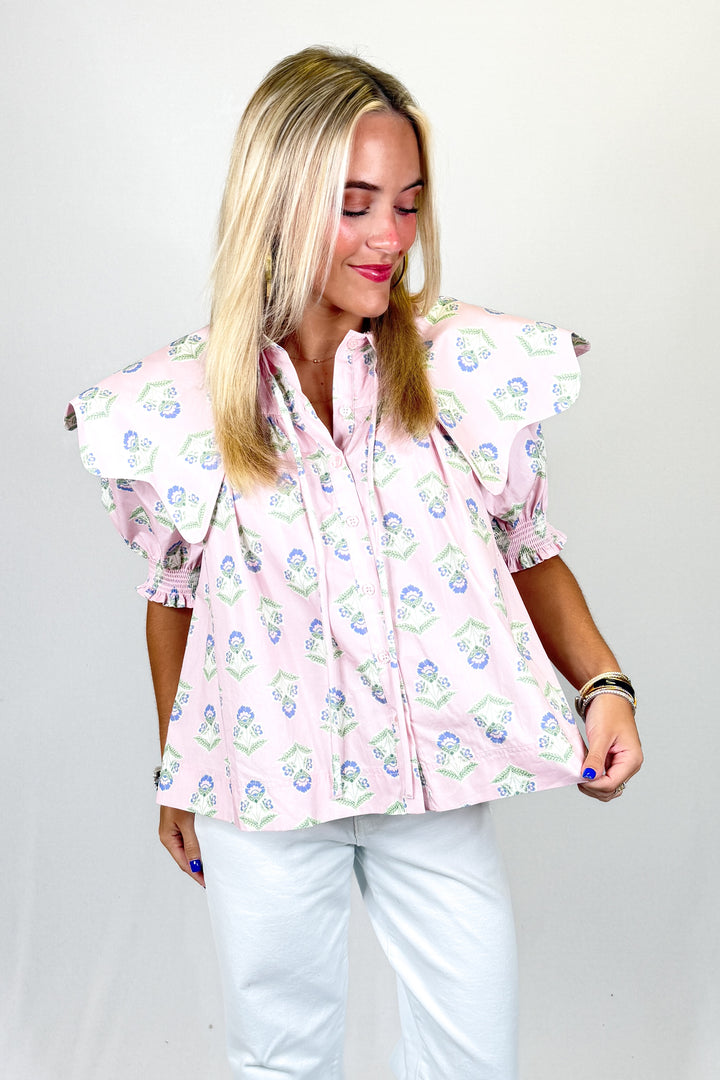 Woman wearing a pink floral blouse with puffed sleeves on a plain background
