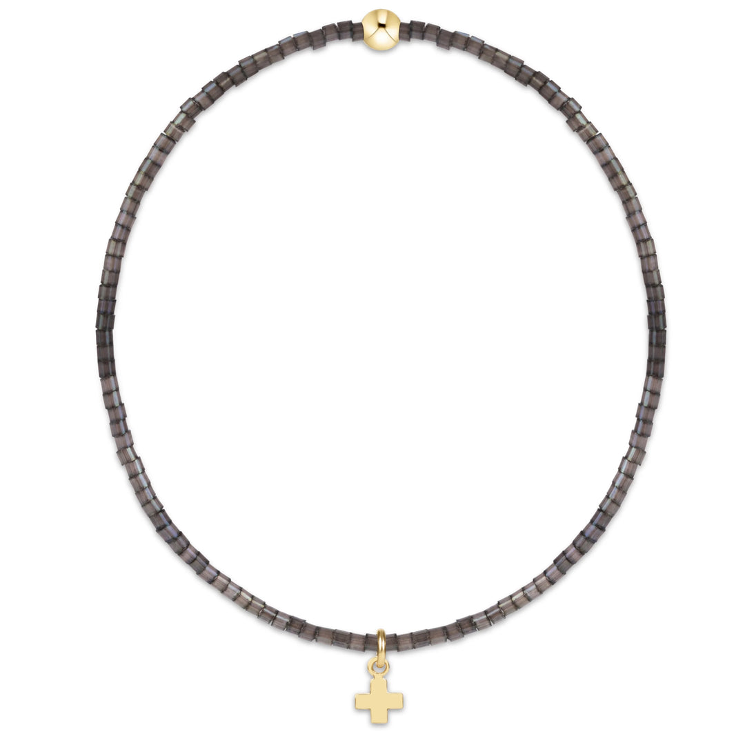 GRAY BEADED BRACELET WITH GOLD CROSS CHARM ON WHITE BACKGROUND