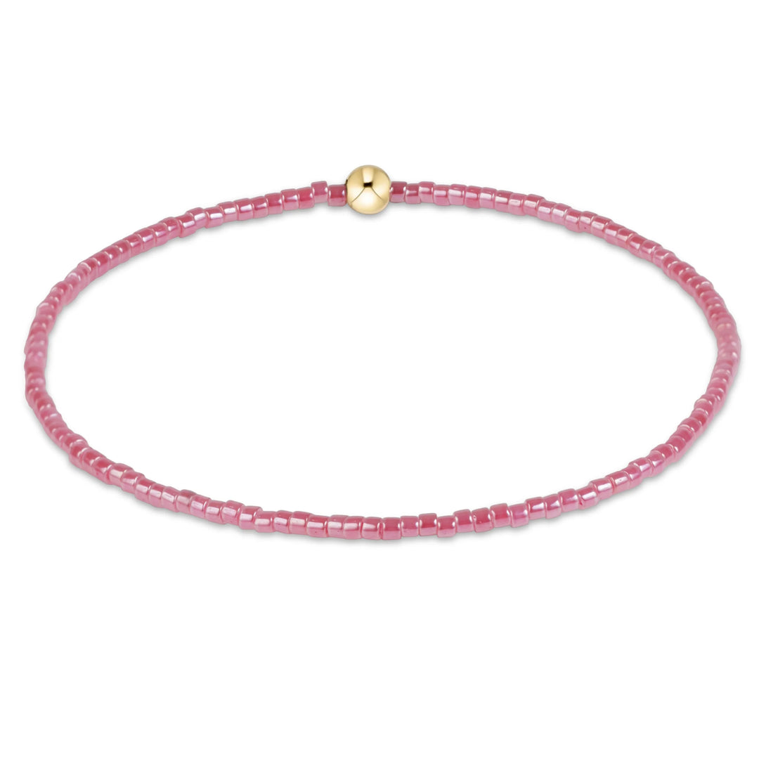 PINK BEADED BRACELET WITH SINGLE GOLD BEAD ON WHITE BACKGROUND