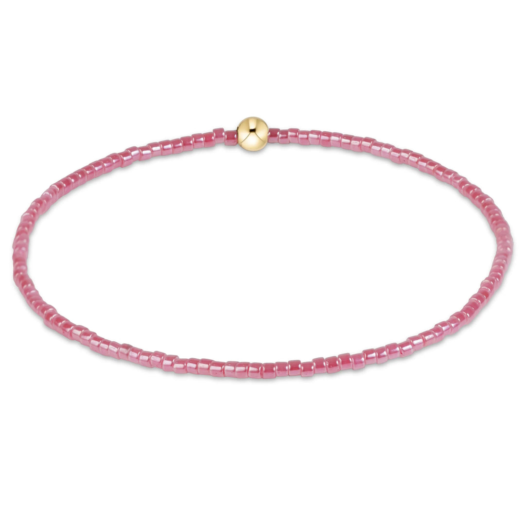 pink beaded bracelet with one gold bead on white background
