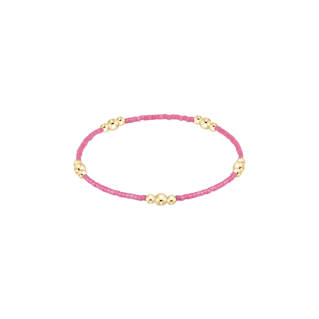 Pink beaded bracelet with gold accents on a white background