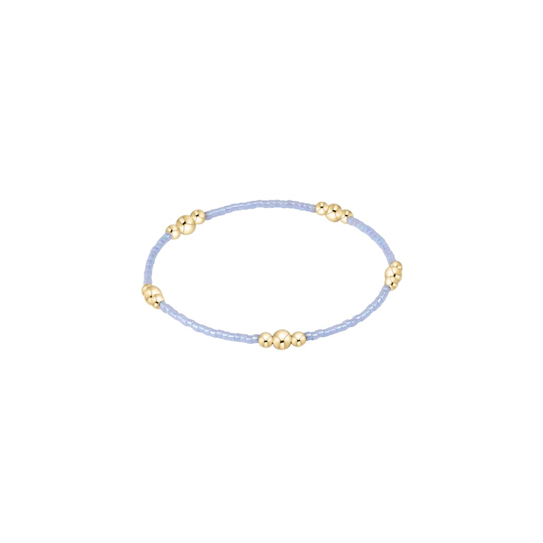 Delicate bracelet with gold beads on a light blue cord against a white background