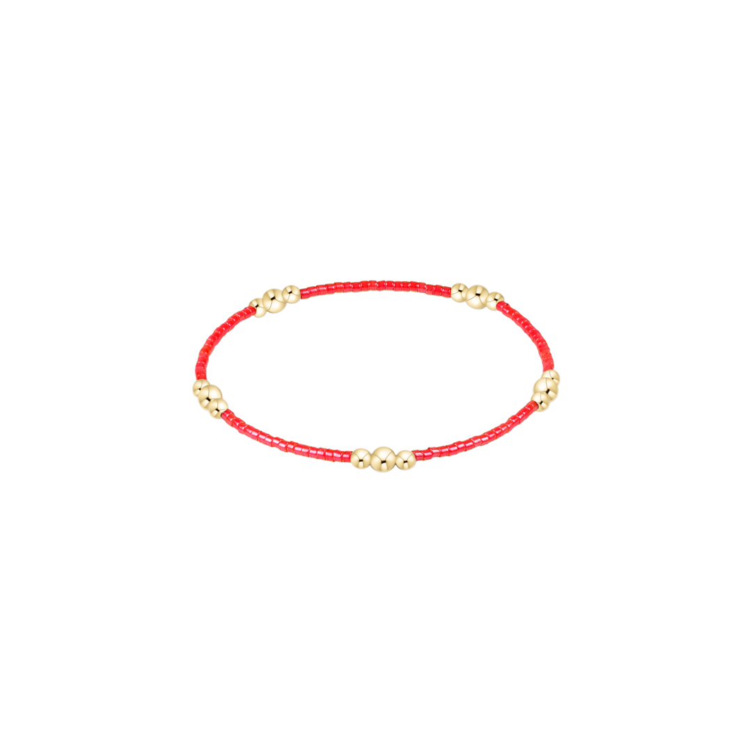 Red beaded bracelet with gold beads on a white background