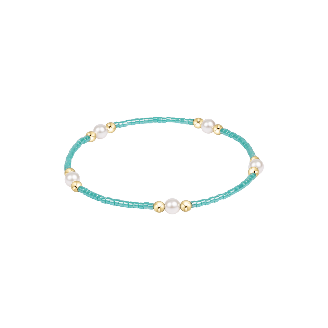 Turquoise beaded bracelet with pearls and gold accents on a white background