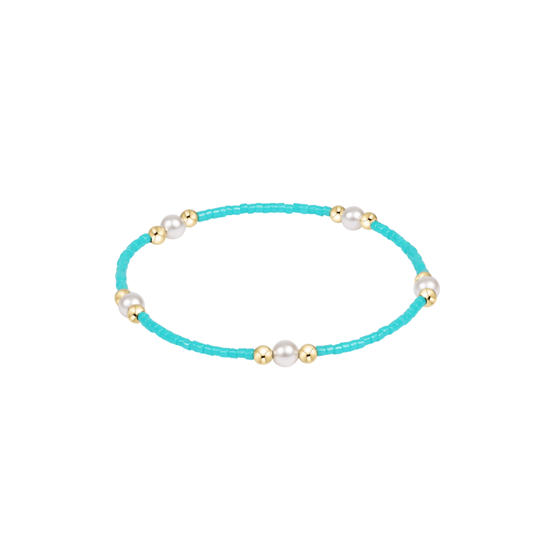 Turquoise bracelet with pearls and gold accents on a white background