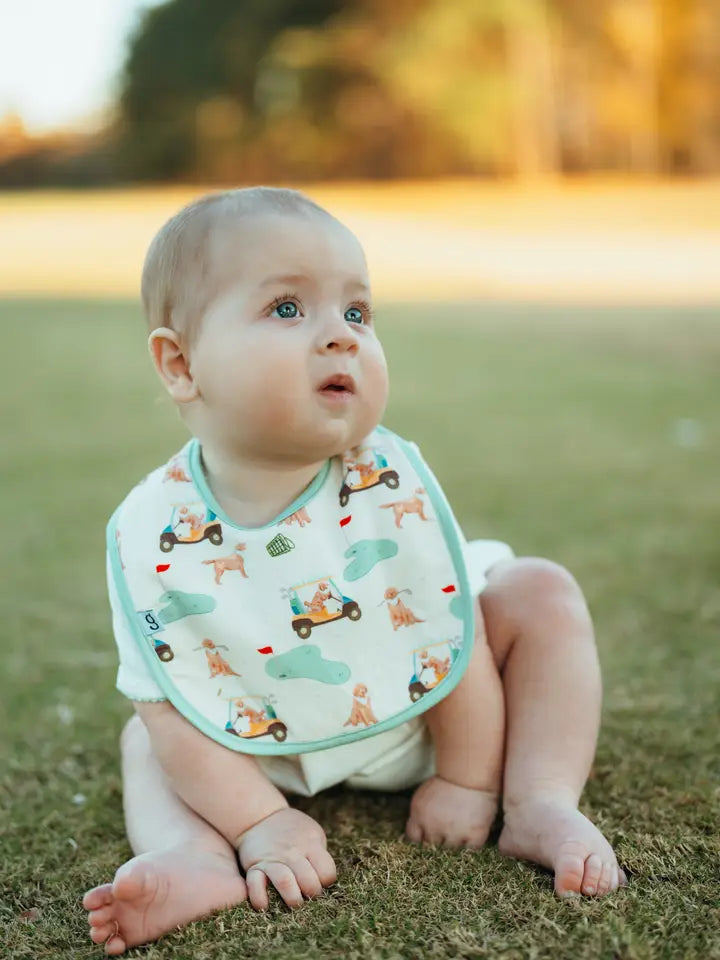 Baby sitting on grass wearing a bib with golf and dog patterns
