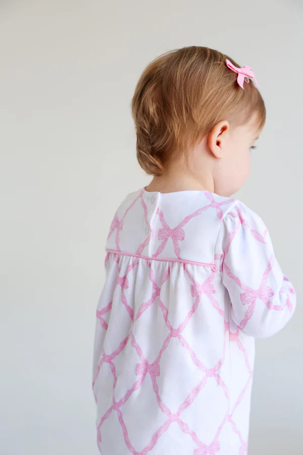 Child wearing a white dress with pink geometric pattern against a plain background