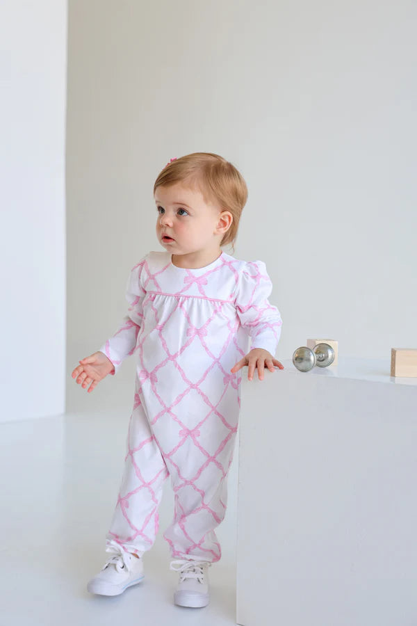 Baby wearing a pink and white patterned outfit standing in a minimalistic room.