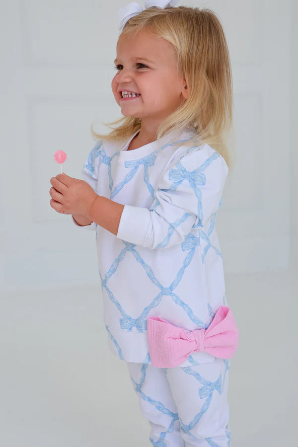 Child wearing a light blue and white patterned outfit with a pink bow, holding a lollipop.