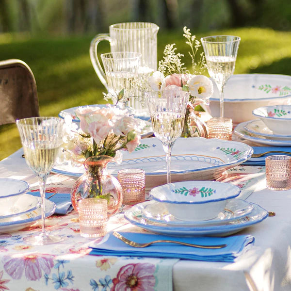 Elegant outdoor table setting with floral tablecloth, glasses, and plates.