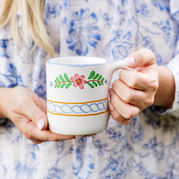 Person holding a decorative mug with floral patterns against a patterned background