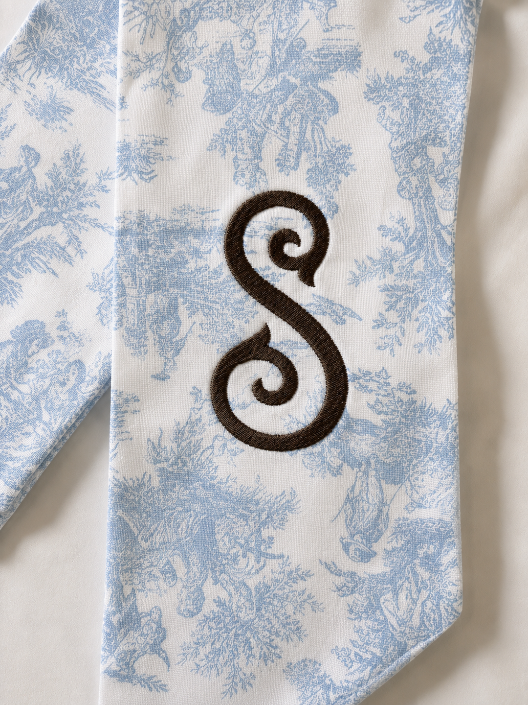 Tie with blue floral pattern and dark brown letter 'S' on a white background