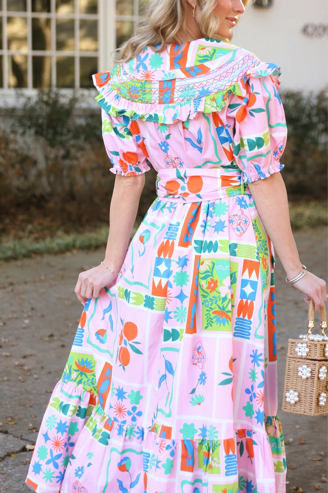 Woman wearing a colorful patterned dress holding a woven handbag.