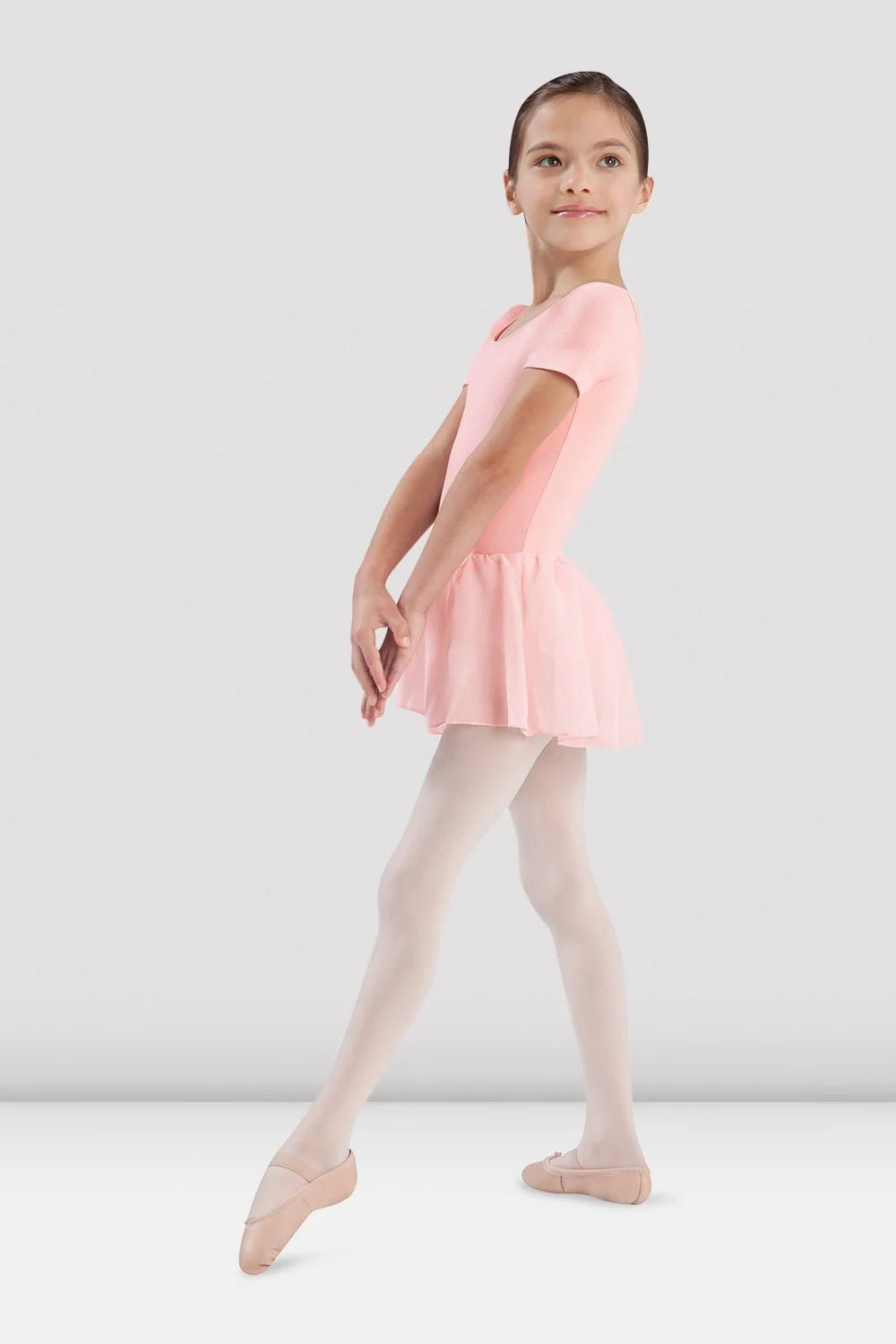 Young girl in a pink ballet dress and tights standing on a white background
