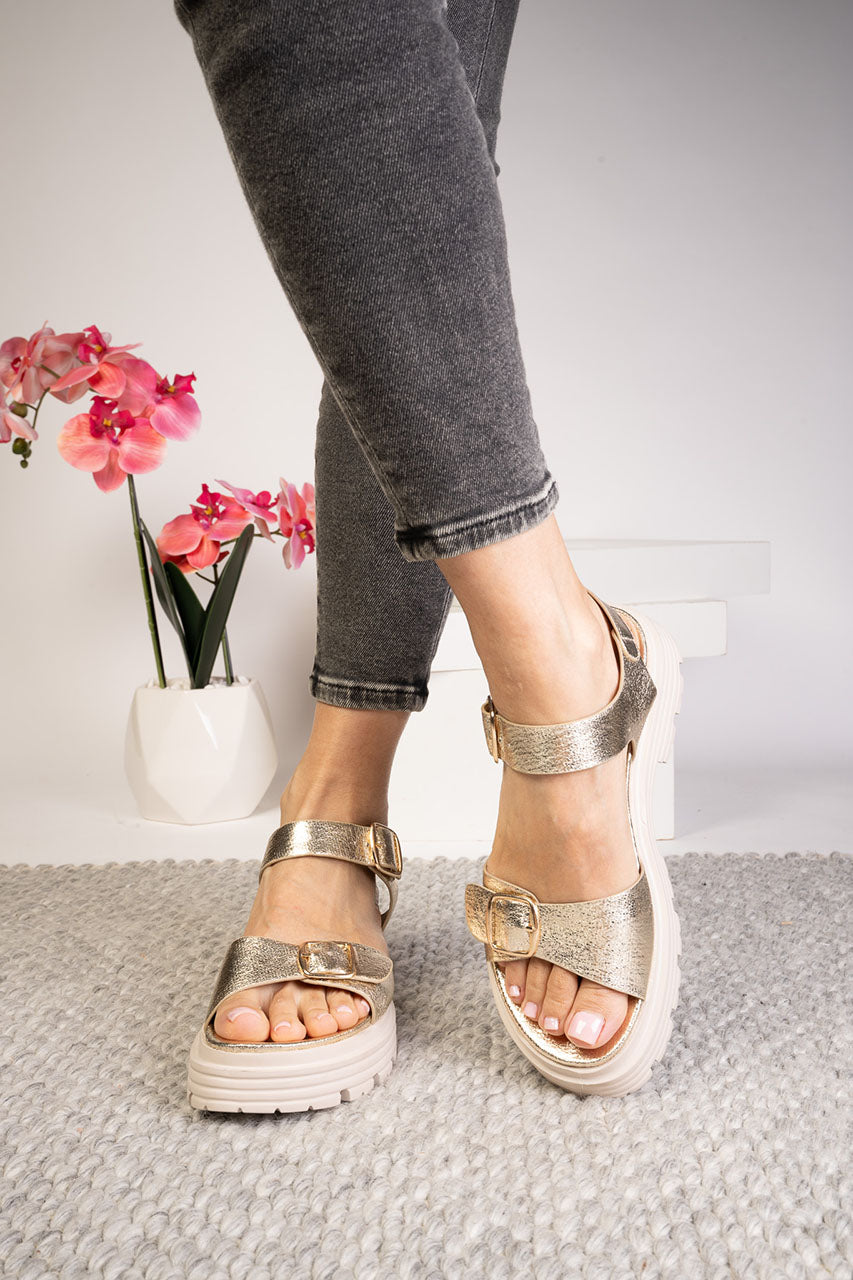 Person wearing silver sandals on a neutral background with flowers in the background