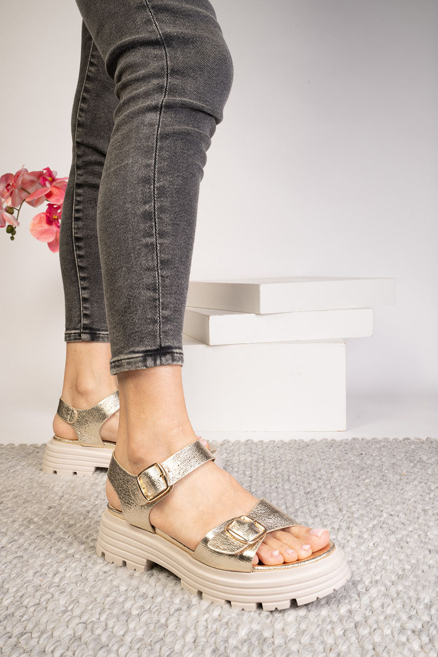 Person wearing metallic platform sandals on a neutral background