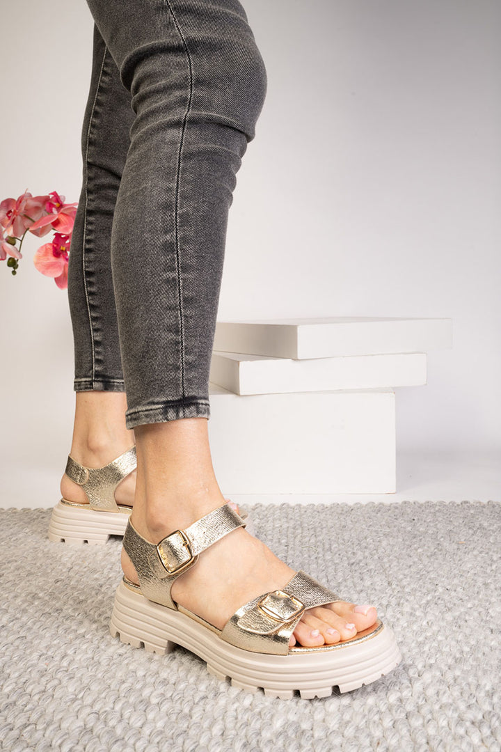 Person wearing metallic platform sandals on a neutral background