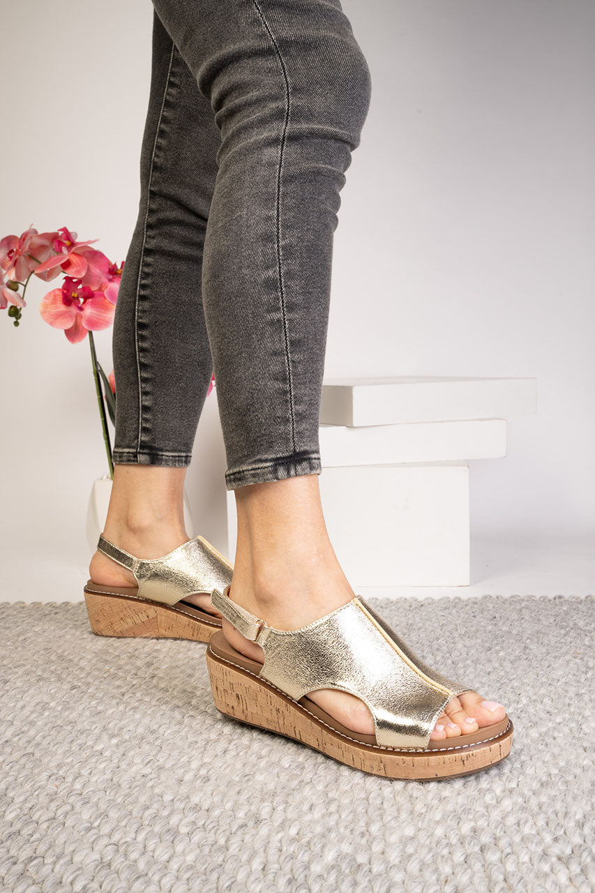 Gold sandals worn with gray jeans on a light background