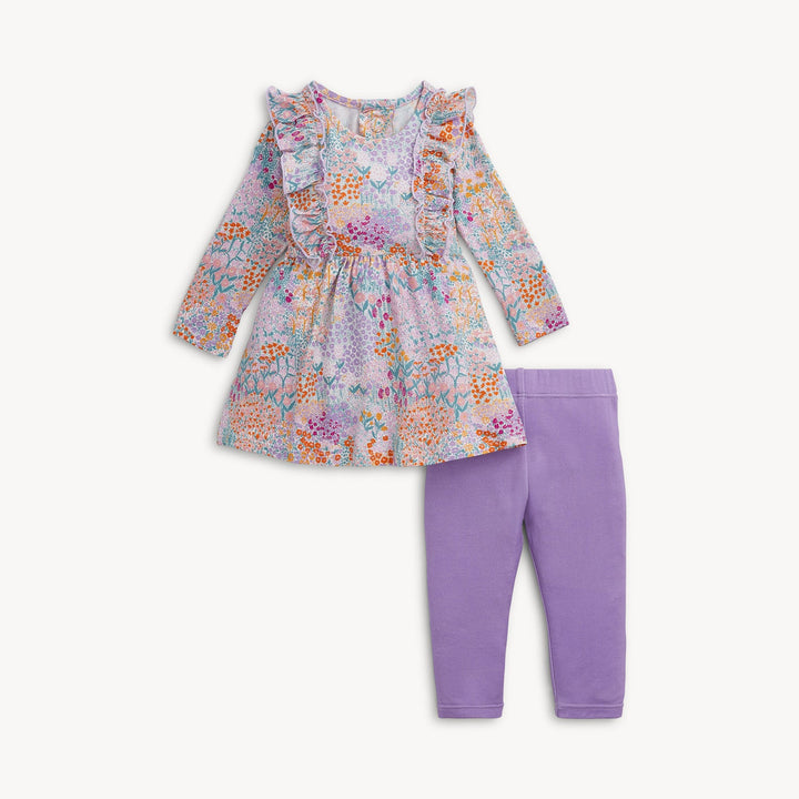 A toddler girl's two-piece outfit set featuring a long-sleeve ruffle-trimmed dress with a multicolor floral and botanical print, paired with solid light purple leggings, shown on a clean off-white background.