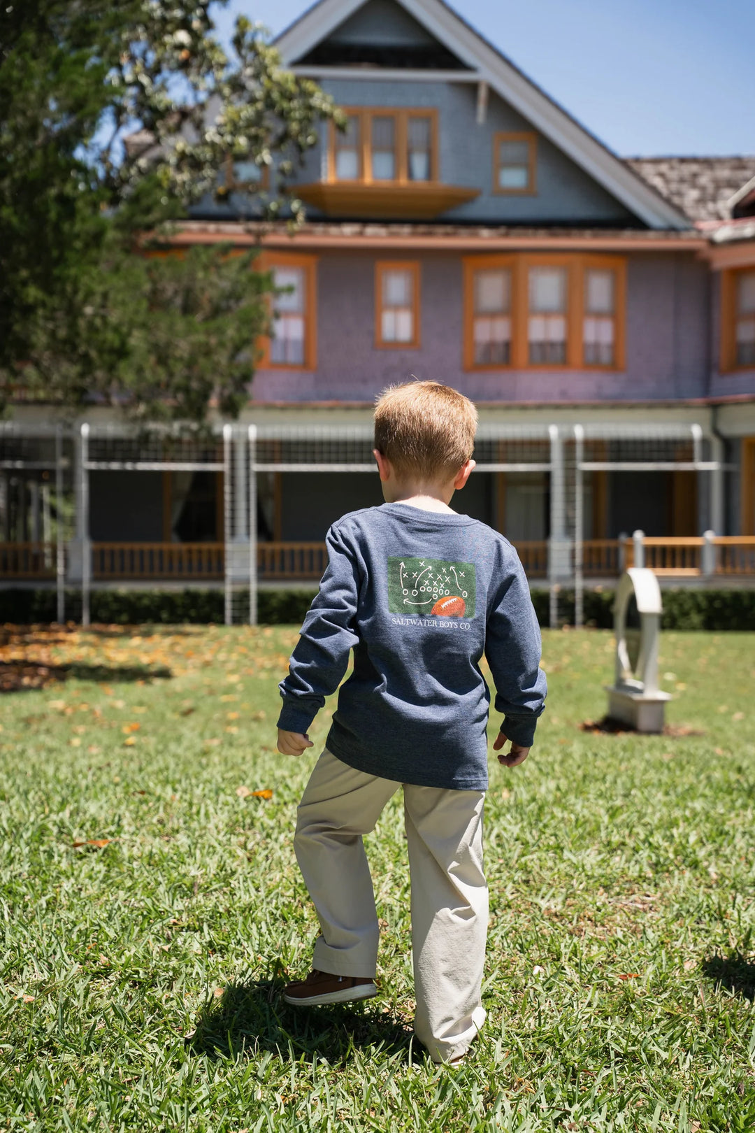 LITTLE BOY WEARING HEATHER BLUE PLAYBOOK LONG SLEEVE GRAPHIC TEE IN GRASSY YARD