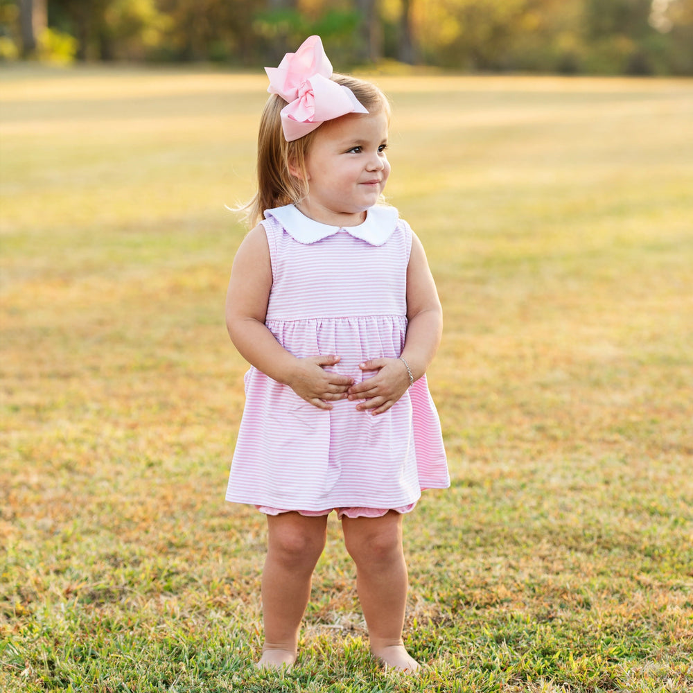 Young girl in a pink dress with a bow standing in a grassy field