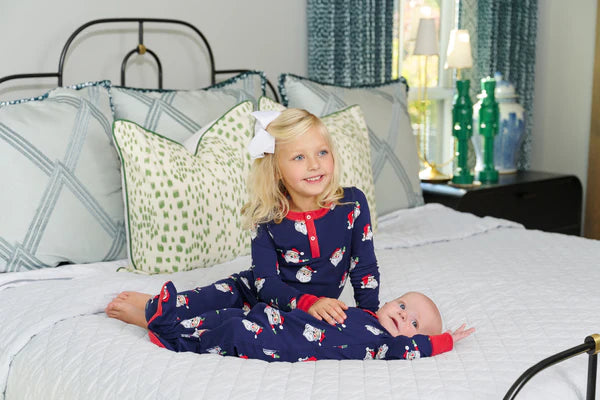 Two children in matching pajamas sitting on a bed with decorative pillows and nightstand.