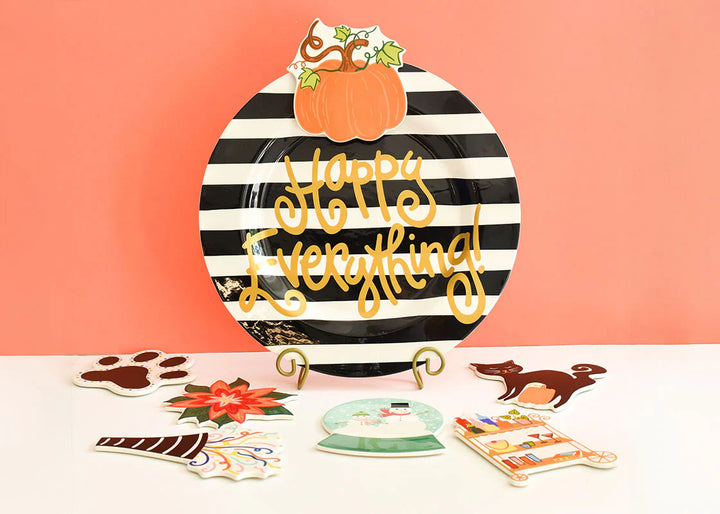 Decorative plate with black and white stripes and 'Happy Everything!' text, surrounded by small decorative items on a pink background.