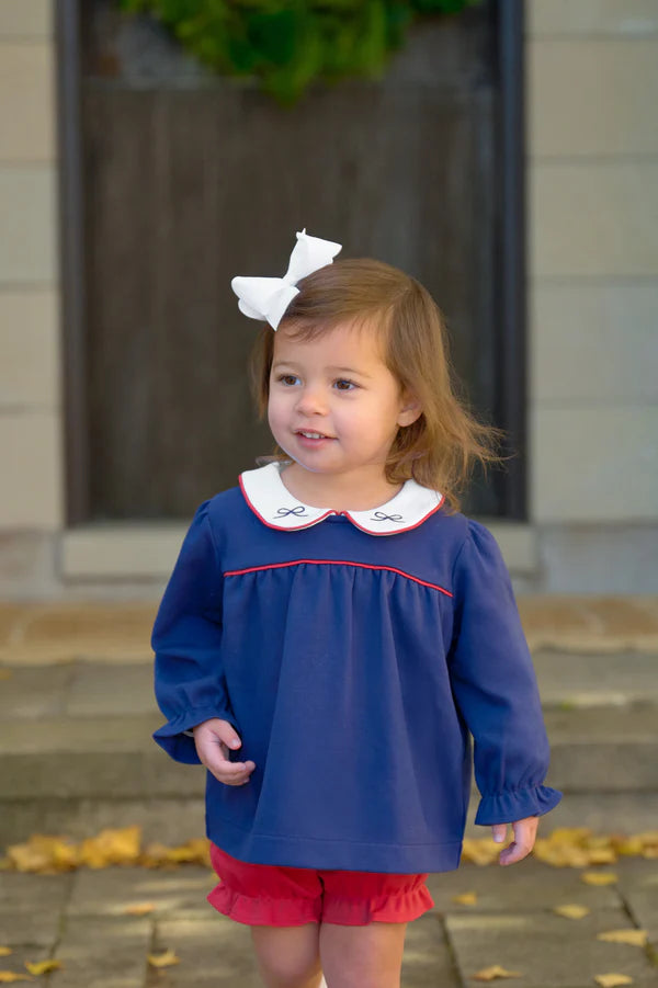 Young girl wearing a blue top with a white collar and red trim, standing outdoors.