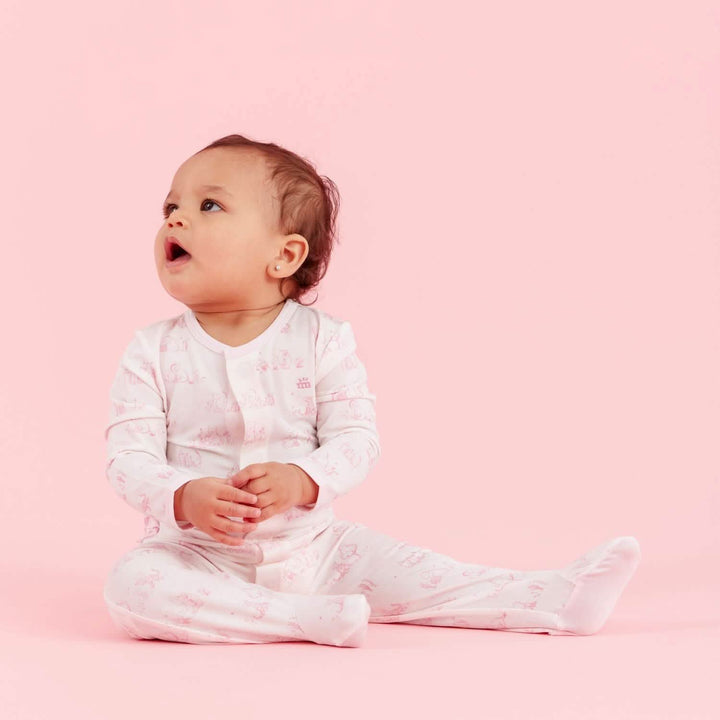Baby in a white outfit with pink patterns sitting on a pink background