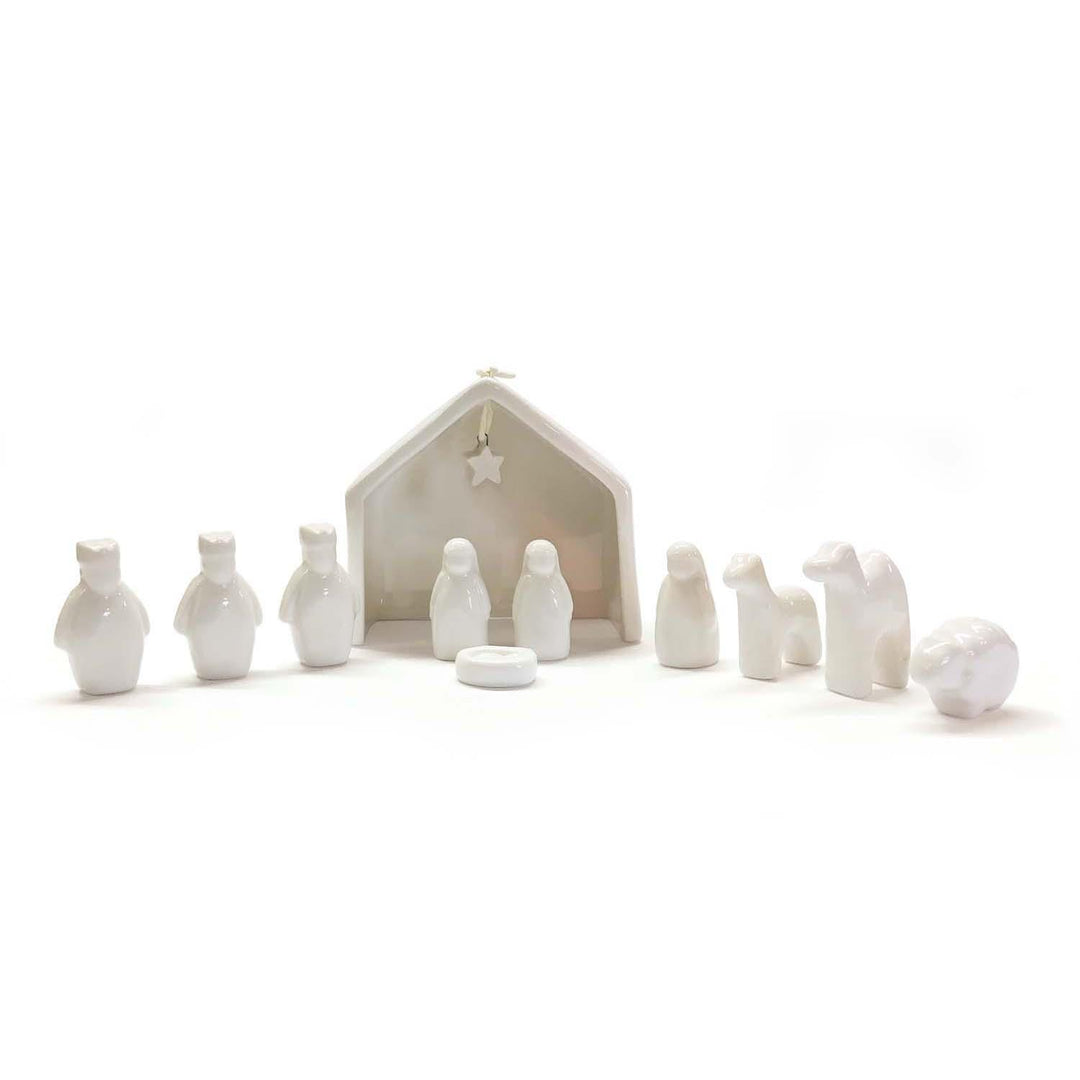 White ceramic nativity set with stable and figures on a white background