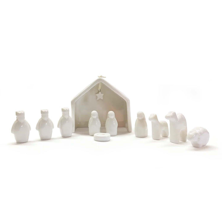 White ceramic nativity set with stable and figures on a white background