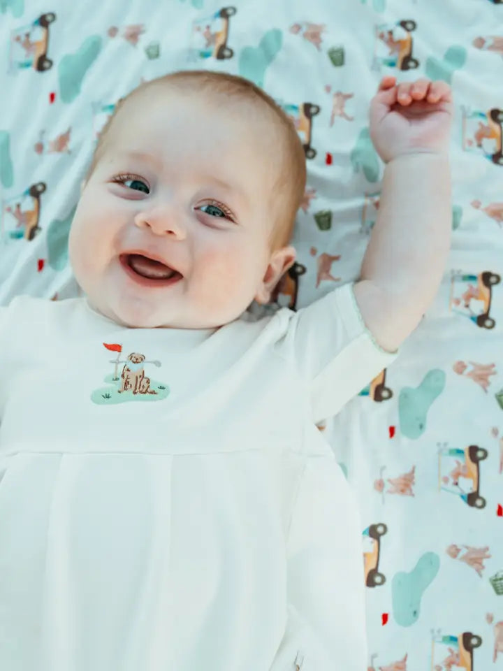 Baby lying on a patterned golf and dog blanket with a smile