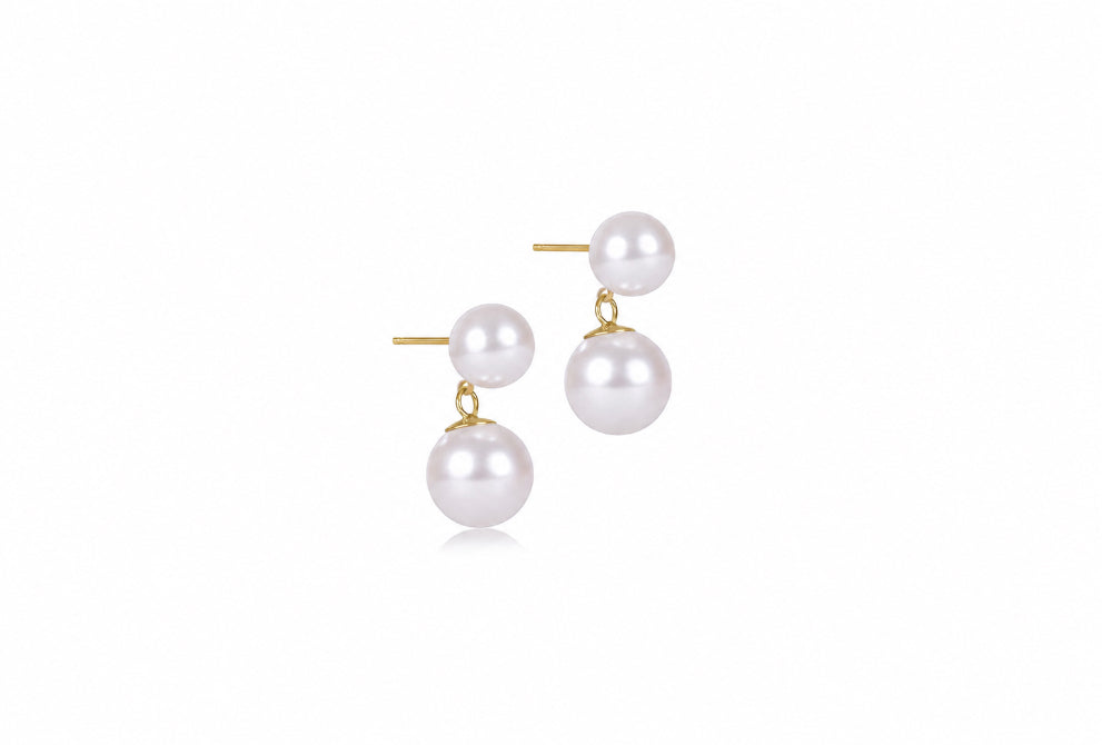 A pair of gold stud earrings featuring two white pearl drops of different sizes, shown on a clean white background.