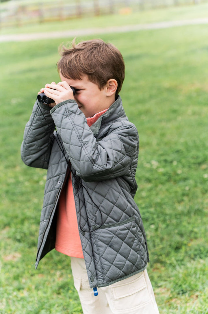 Child in a dark green quilted jacket standing outdoors on grass