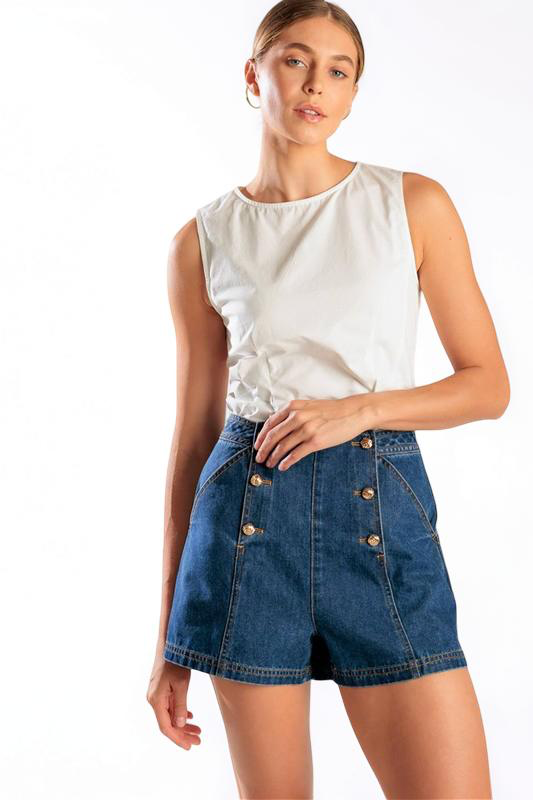Woman wearing a white sleeveless top and blue denim shorts on a white background