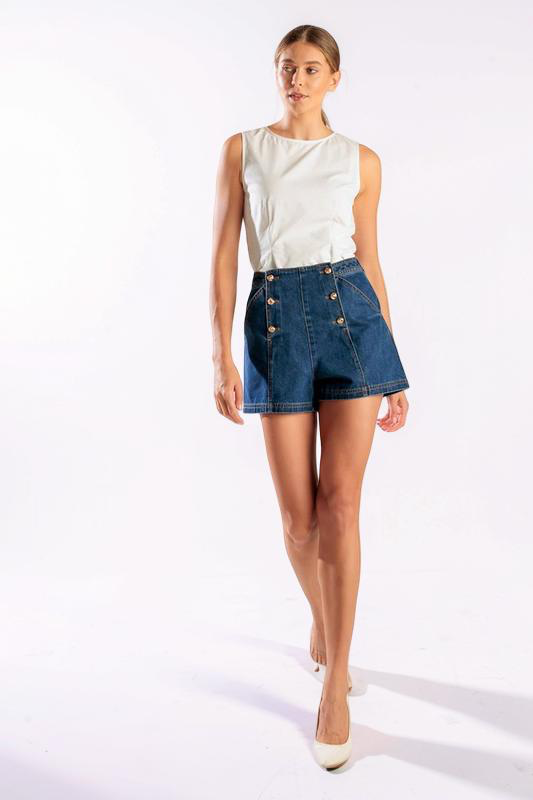 Woman wearing a white sleeveless top and blue denim shorts on a white background