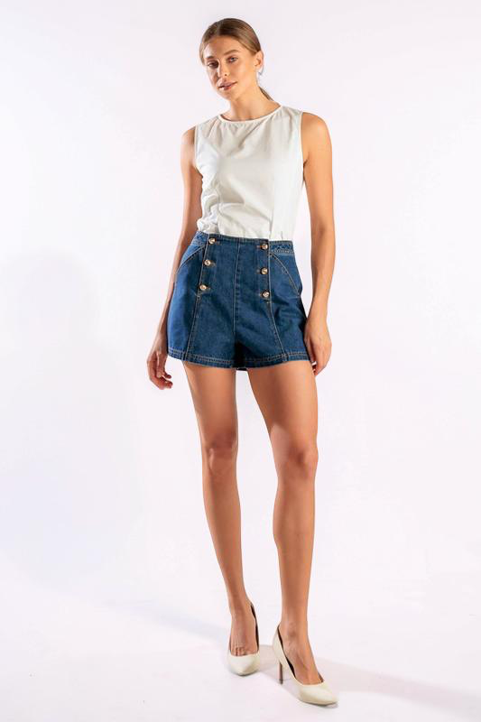 Woman wearing a white sleeveless top and blue denim shorts with buttons on a white background