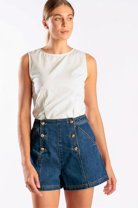 Woman wearing a white sleeveless top and blue denim shorts with gold buttons on a white background