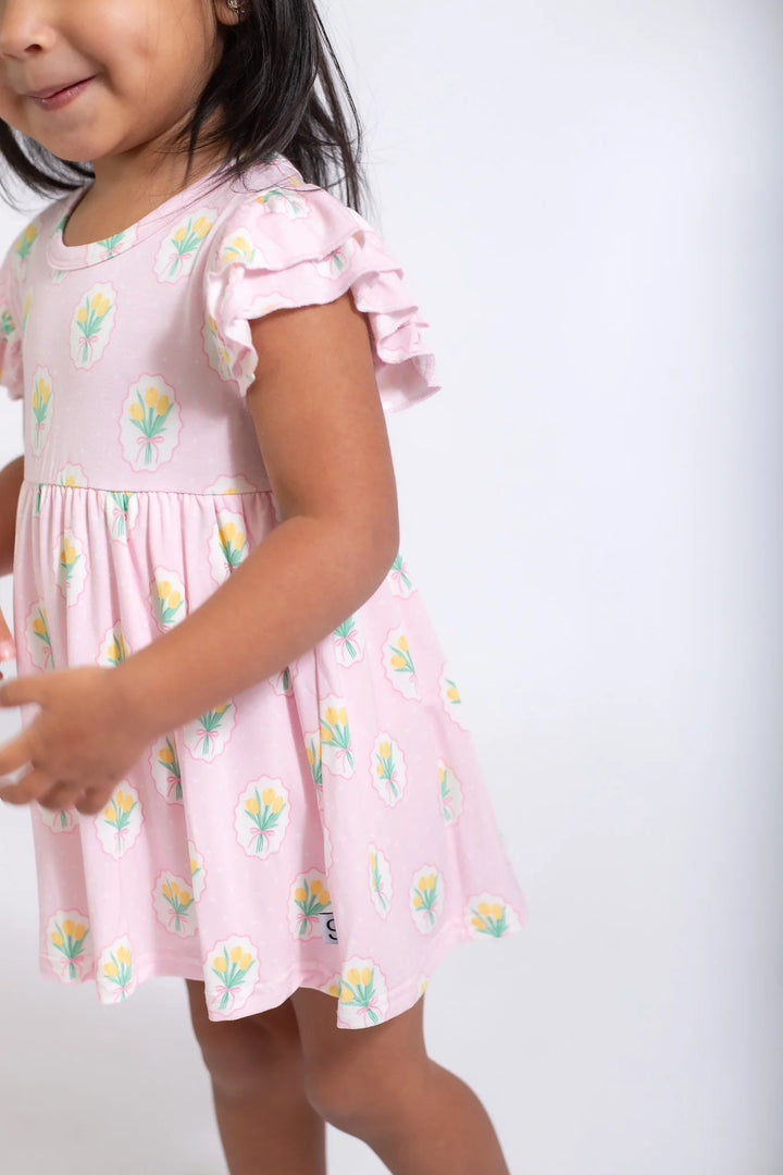 Child wearing a pink dress with floral patterns on a white background
