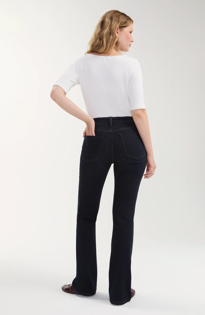 A woman shown from the back wearing a white short-sleeve top and dark black flare jeans against a light gray studio background.