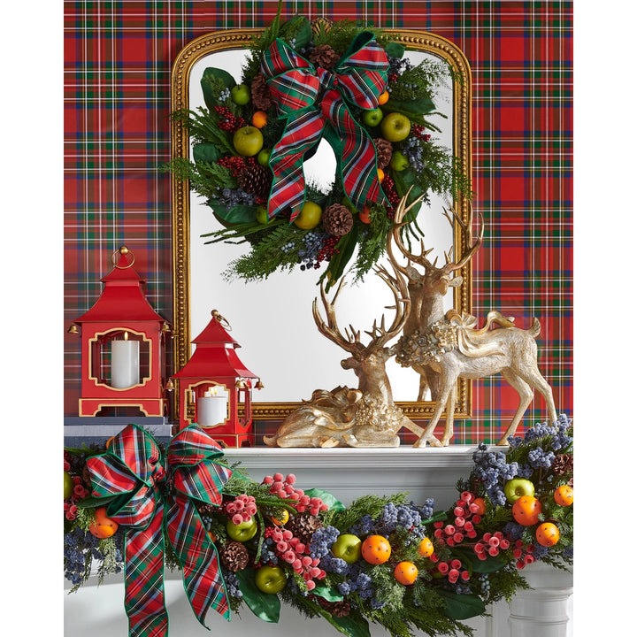 Decorative Christmas mantel with wreath, garland, and figurines against a plaid background