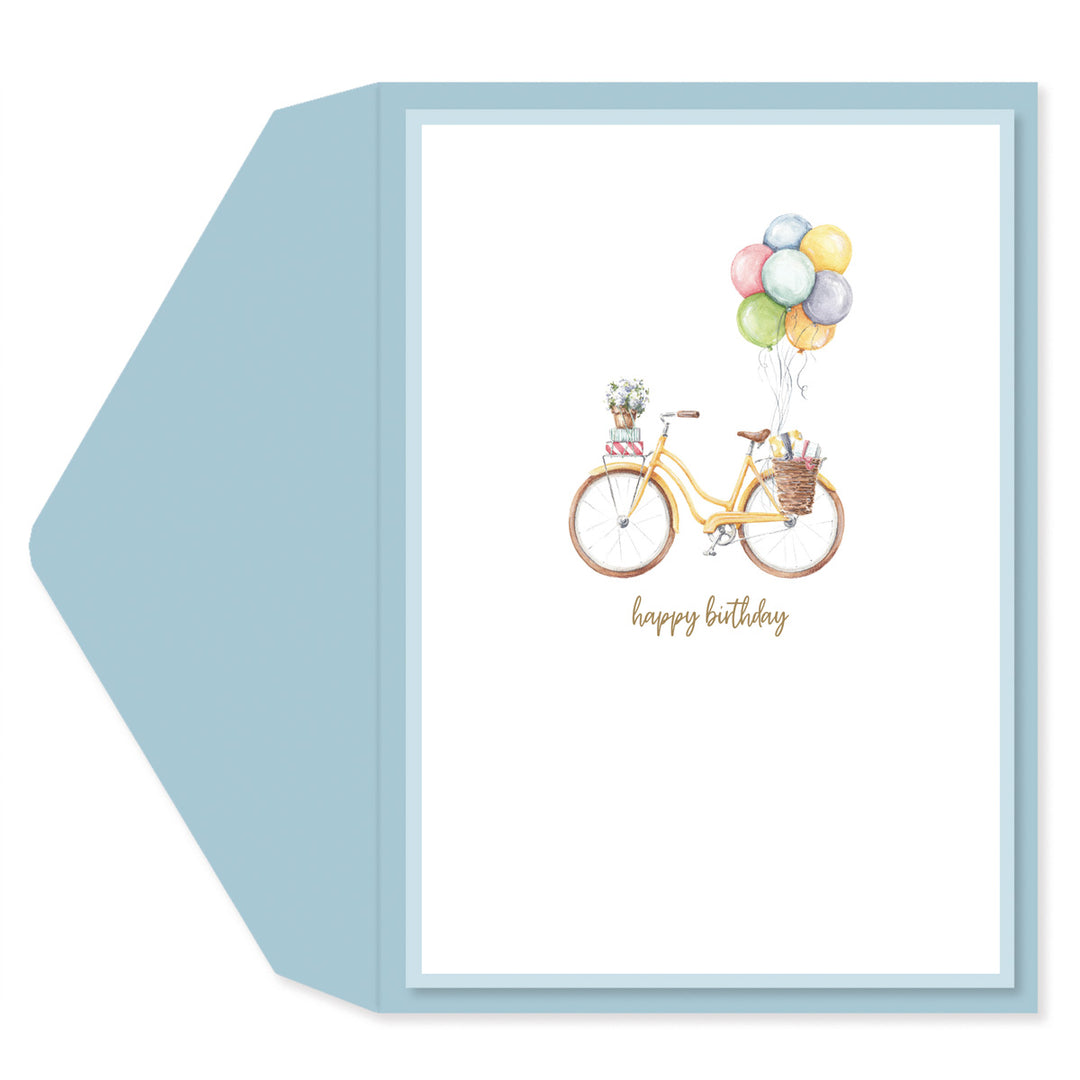 A square greeting card with a light blue envelope behind it. The card features a watercolor illustration of a yellow bicycle with a basket of colorful balloons and the words 'happy birthday' in gold script.